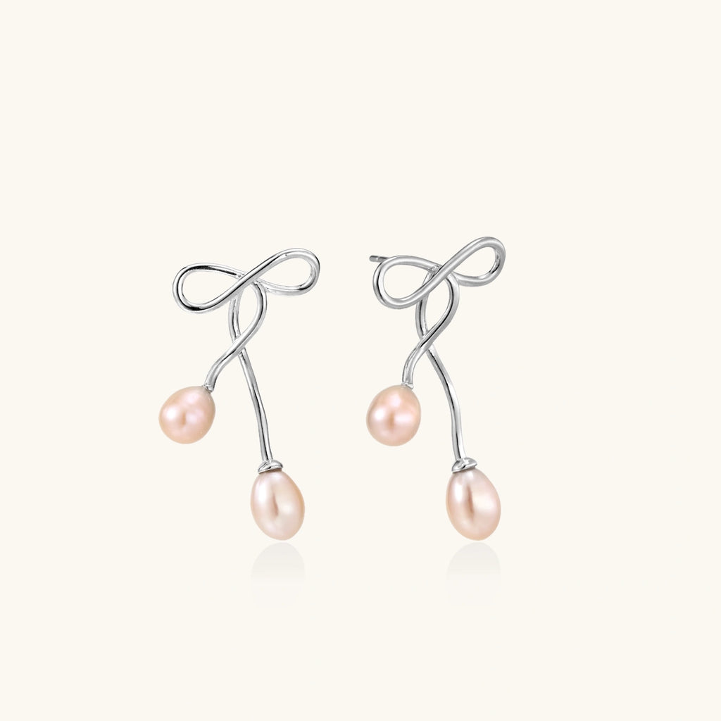Rhodium-plated silver earrings with organic vine curves and two peachy freshwater pearls on cream background