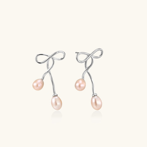 Rhodium-plated silver earrings with organic vine curves and two peachy freshwater pearls on cream background