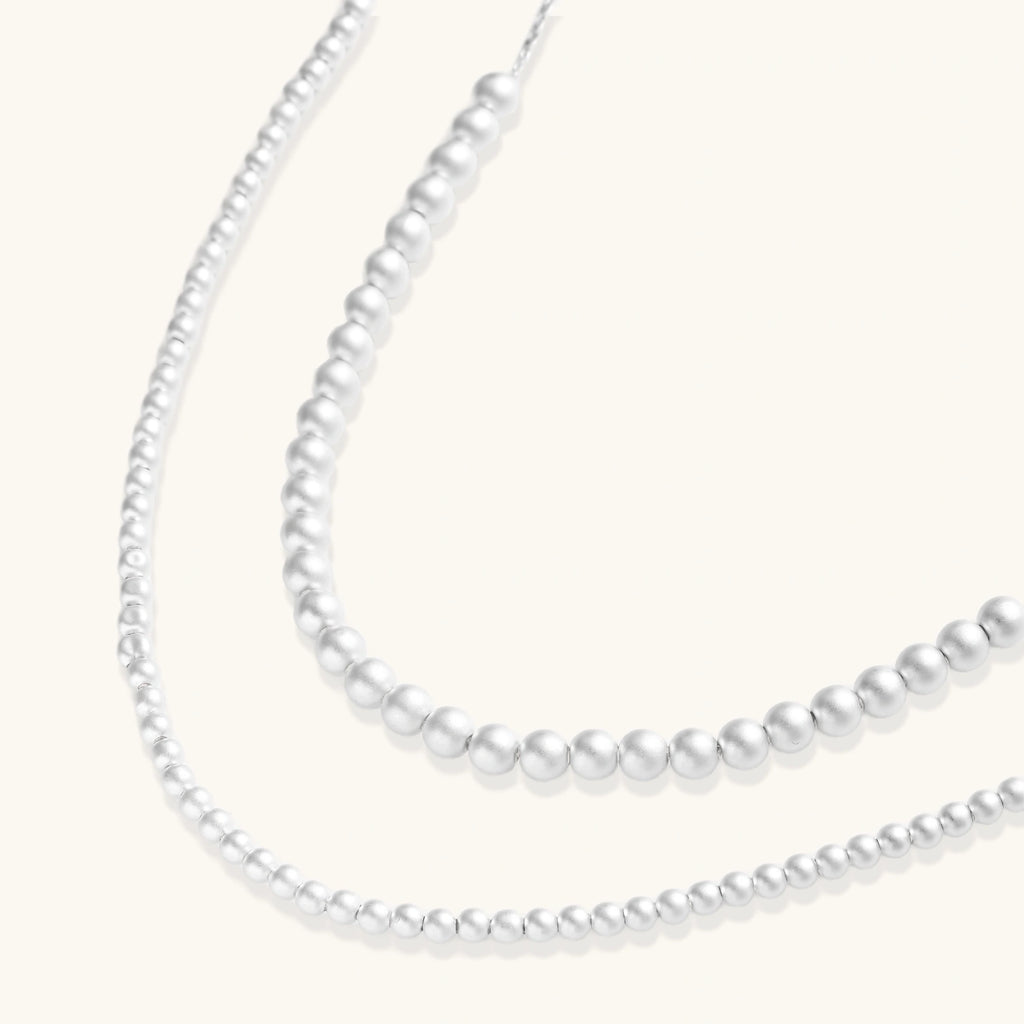 Long sterling silver beaded necklace with graduated sphere design, toggle clasp, and delicate chain extension on white background